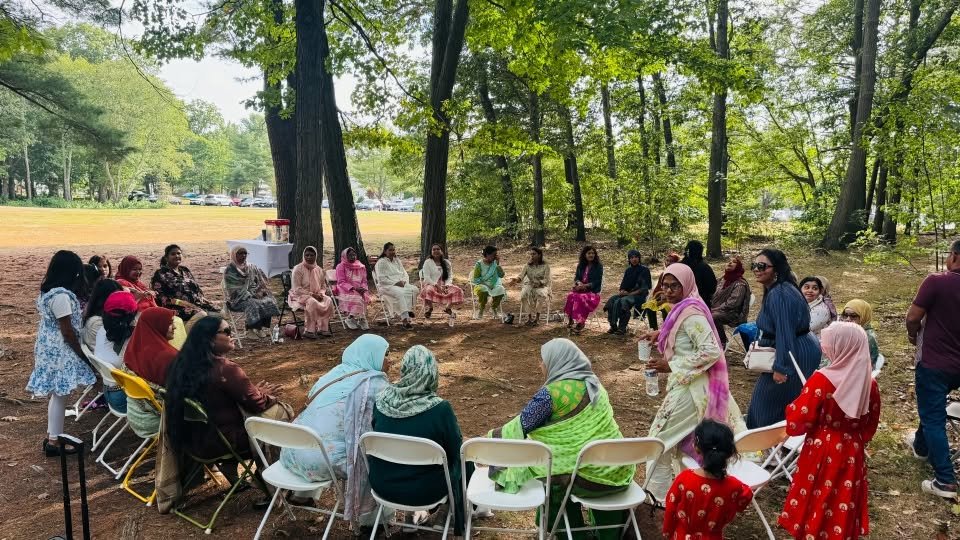 Guests seated in a circle of folding chairs on the shaded lawn.